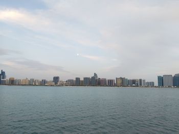 Sea by buildings in city against sky