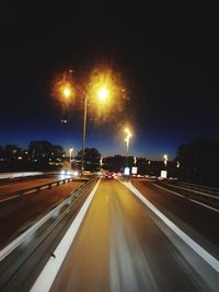 Illuminated street lights on road against sky at night