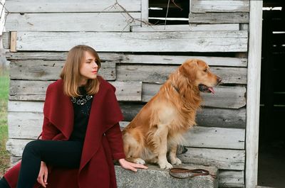 Young woman sitting with dog on bench outside house