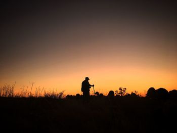 Silhouette man standing on field against orange sky