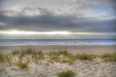 View of calm beach against cloudy sky