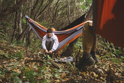 A man sitting in a hammock in the forest gets prepared for hiking