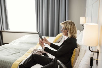 Side view of businesswoman using digital tablet sitting on bed at hotel room