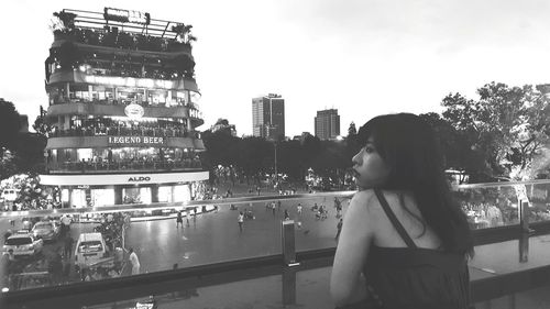 Woman standing by railing in city against sky