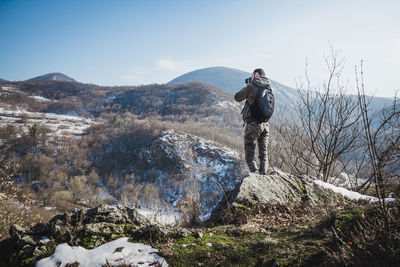 Rear view of man standing on mountain against sky