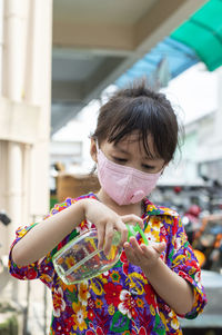Cute girl wearing mask using hand sanitizer outdoors