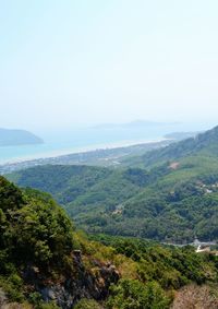 Scenic view of green landscape and sea against clear sky
