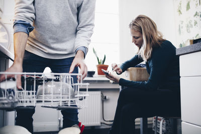 Midsection of man working in kitchen with woman using mobile phone at home