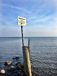 Information sign on wooden post by sea against sky