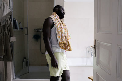 Mentally exhausted man with towel leaning on bathroom wall at home