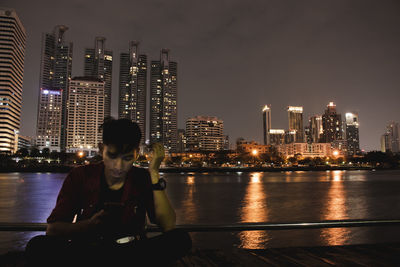 Man using phone sitting against railing in city at night