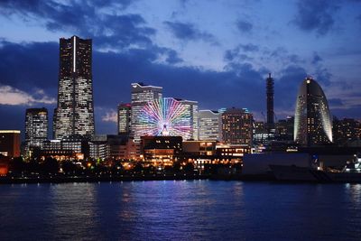 Illuminated city by river against sky at night