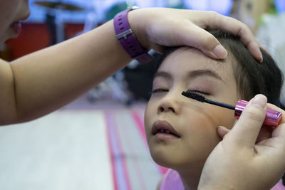 Cropped hand of mother applying mascara on daughters eyes