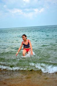 Carefree young woman splashing water in sea against sky