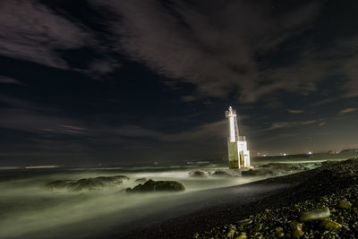 Lighthouse by sea against sky at night