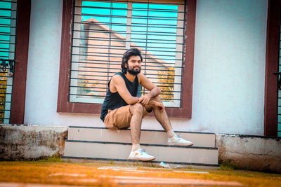 Full length of young man sitting against wall