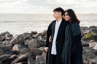 Lesbian women embracing while standing on rock against sea and sky