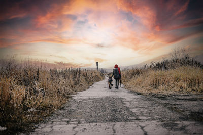 Rear view of men walking on road against sky during sunset