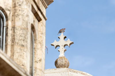 Low angle view of cross by building against sky