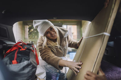 Smiling mature woman loading cardboard in car trunk