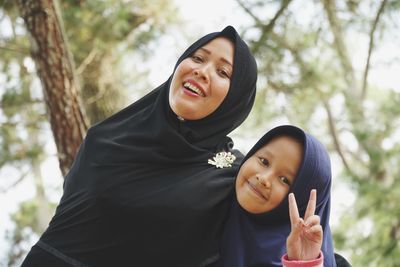 Portrait of smiling woman and daughter gesturing against trees