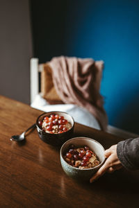 Cropped hand holding bowl with breakfast on table