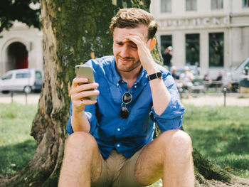 Young man using mobile phone while sitting on tree