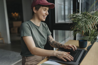 Happy businesswoman with tattooed arm working on laptop at home