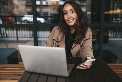 Portrait of smiling woman using phone while sitting at table