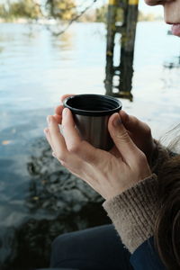 Midsection of woman holding coffee cup by lake