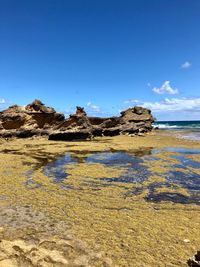 Scenic view of rocks on beach against blue sky