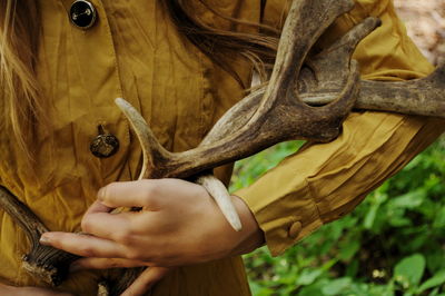 Midsection of woman holding antler while standing in forest