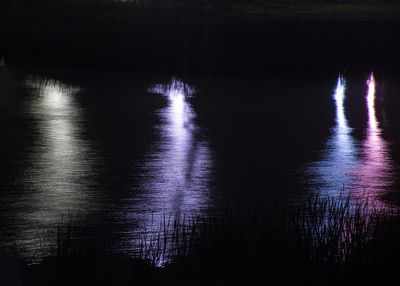 Silhouette trees by lake against sky at night