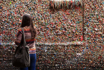 Rear view of young woman standing against gum wall