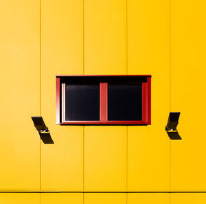 Low angle view of window amidst security cameras of yellow wall