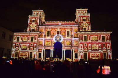 People at illuminated building against sky at night