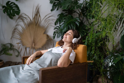 Girl florist in headphones relax in indoor garden listening to music after work and care for plants