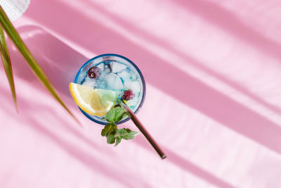 Top view of refreshing blue curacao cocktail on pink background garnished with mint and lemon slice.