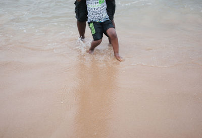 Low section of man walking on wet beach