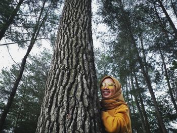 Smiling young woman standing by tree trunk in forest
