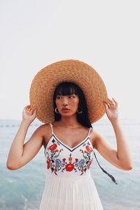 Young woman wearing hat standing at beach against sky