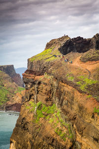 Cliff by sea against cloudy sky