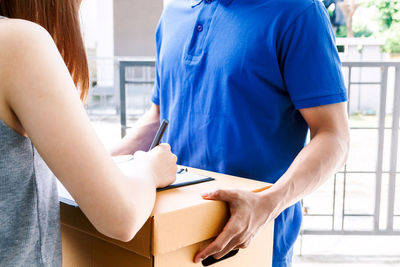 Midsection of woman signing paper while delivery person holds package