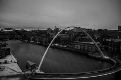 Bridge over river by buildings in city against sky