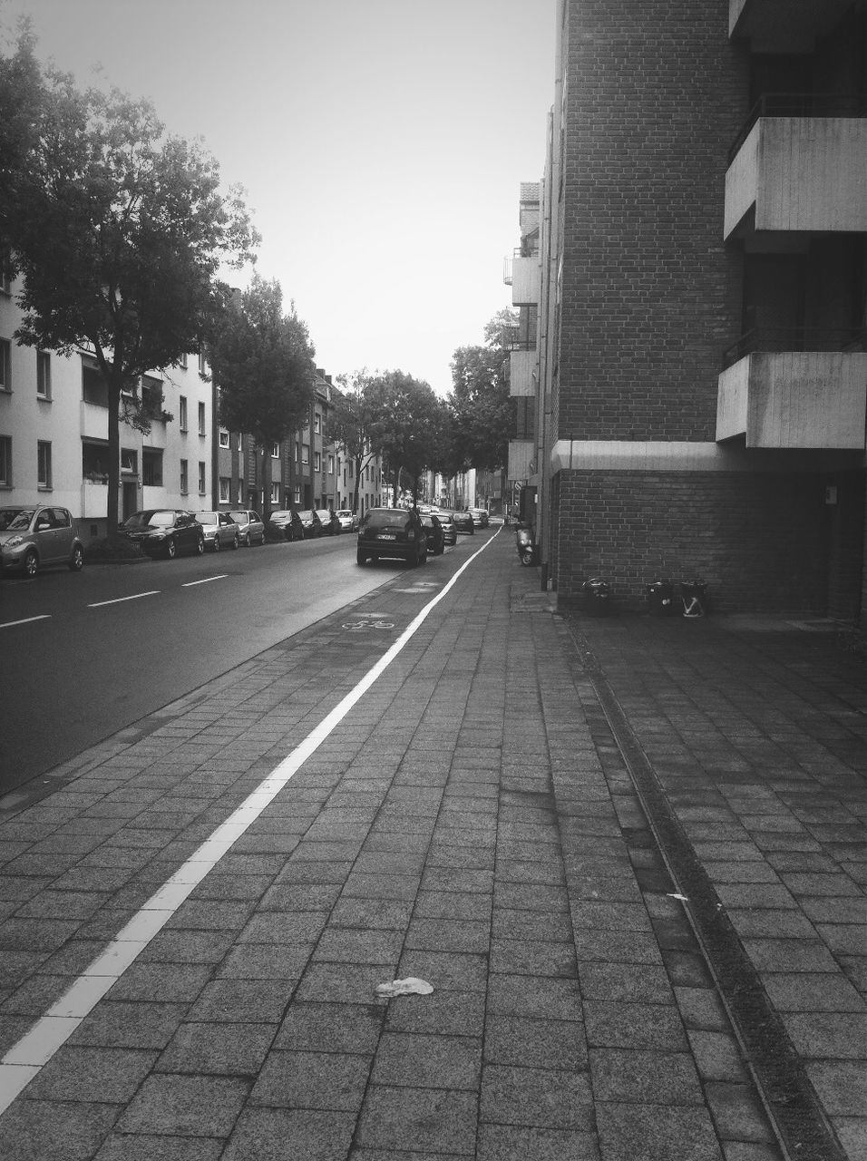 building exterior, architecture, built structure, transportation, the way forward, street, city, road, diminishing perspective, car, road marking, tree, building, clear sky, vanishing point, land vehicle, incidental people, city life, mode of transport, city street