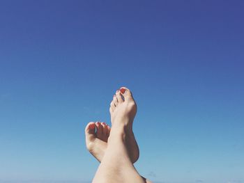 Low section of woman with feet up against blue sky
