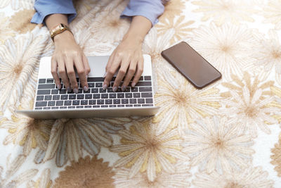 Cropped hands of woman using laptop on bed at home