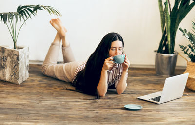 Young woman using smart phone while sitting on laptop
