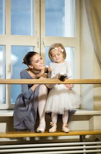 A little ballerina ties pointe shoes to an adult ballerina.