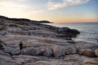 Scenic view of rocks at beach against sky during sunset